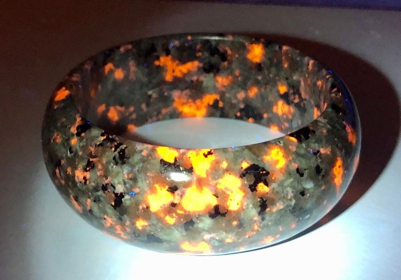 May include: A dark green and black bracelet with orange flecks. The bracelet is made of a natural stone and has a smooth, polished finish.