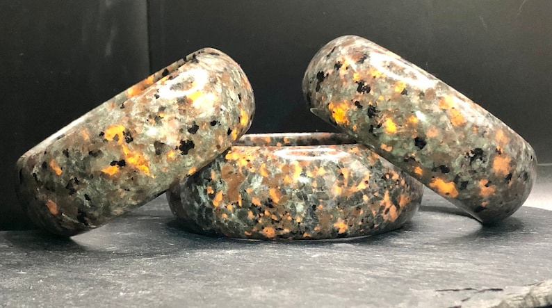 May include: Three polished stone bracelets with a mottled green, black, and copper color pattern.
