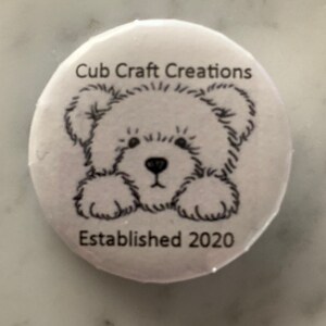 Könnte beinhalten: Weißer Knopf mit einer Schwarzweißillustration eines Teddybären und dem Text "Cub Craft Creations Established 2020".