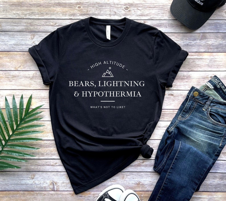 May include: Black t-shirt with white text that reads "HIGH ALTITUDE - BEARS, LIGHTNING & HYPOTHERMIA WHAT'S NOT TO LIKE?"