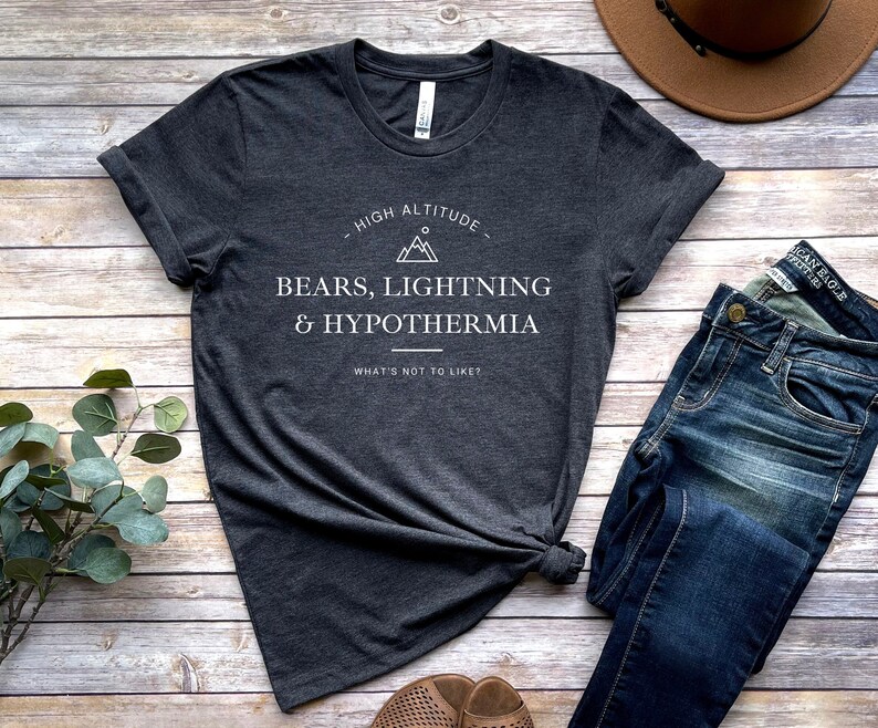 May include: A dark gray t-shirt with a white graphic that says "High Altitude - Bears, Lightning & Hypothermia - What's not to like?" The graphic also includes a mountain range and a sun.