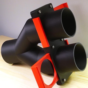 Peut inclure: Un raccord en Y en plastique noir avec deux tuyaux en plastique noir qui s'étendent du haut. Les tuyaux sont munis de poignées en plastique rouge.