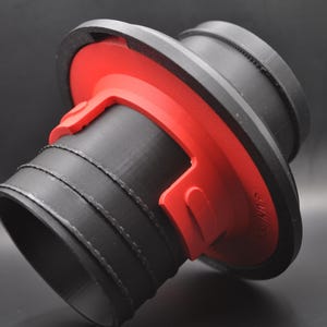 Könnte beinhalten: Ein schwarzer und roter Kunststoffadapter mit einer runden Öffnung und einem gerippten Design. Der Adapter hat eine rote Kunststofflasche, die zum Befestigen verwendet werden kann.