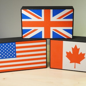May include: Three black rectangular boxes with flags of the United Kingdom, the United States, and Canada. The UK flag is on top, the US flag is on the left, and the Canadian flag is on the right. The flags are in their respective colors.