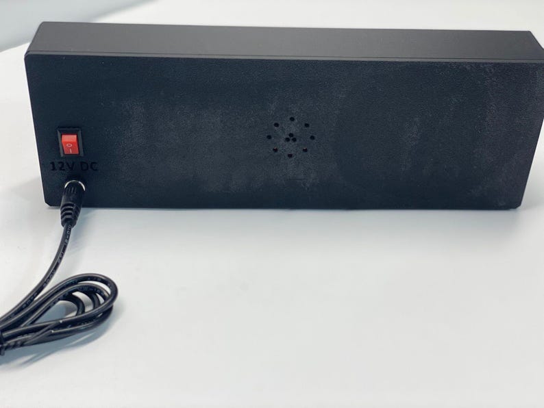 Puede incluir: Un dispositivo electr&oacute;nico rectangular negro con un interruptor de encendido rojo y una entrada de 12V CC. El dispositivo tiene una serie de peque&ntilde;os agujeros y un cable de alimentaci&oacute;n.