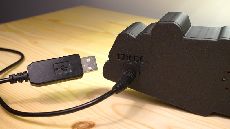 Puede incluir: Un dispositivo electr&oacute;nico negro con un cable USB conectado. El dispositivo tiene el texto "12V DC" impreso. El cable USB est&aacute; conectado a un puerto USB.