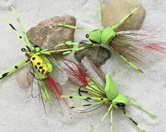 Può includere: Tre esche da pesca a mosca verde e gialle con accenti in bianco e nero. Le esche hanno un corpo in schiuma e sono legate con piume e altri materiali.