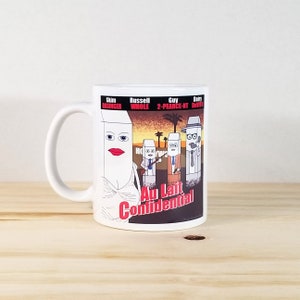 May include: White ceramic coffee mug featuring a cartoon illustration with the text "Au Lait Confidential." The design includes anthropomorphic milk cartons with various labels and names. The mug has a curved handle.