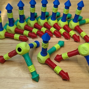 May include: A collection of colorful, plastic toy construction pieces. Each piece features a combination of red, green, yellow, and blue, with a unique shape and design. The toys are arranged on a wooden surface.