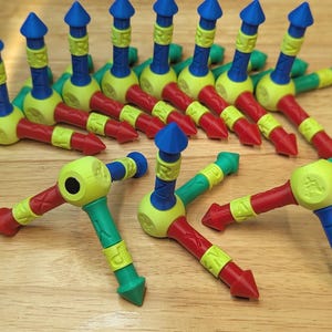 May include: A collection of multi-colored plastic building components featuring a central yellow sphere with protruding arms in red, blue, and green. Each arm is tipped with a pointed cone and features embossed letters including X, Y, Z, and P.