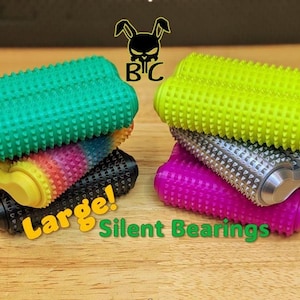 May include: Two stacks of cylindrical fidget rollers with spiked textures. The left stack features green, rainbow-patterned, and black rollers. The right stack includes neon yellow, silver, and purple rollers. Text reads Large! Silent Bearings.
