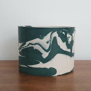 May include: A cylindrical planter with a marbled design. The planter features a dark teal and off-white swirl pattern. The planter is sitting on a wooden surface against a white background. The planter is approximately 15 cm tall.