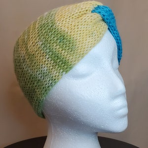 May include: A green, yellow, and blue knitted headband with a knotted design. The headband is on a white mannequin head.