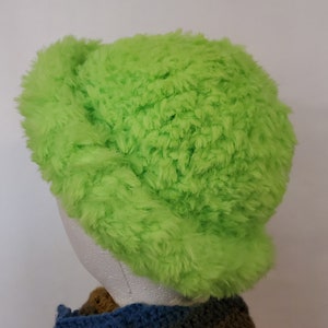 Pode incluir: Um chapéu verde brilhante e felpudo com uma aba larga. O chapéu é feito de um material macio e felpudo e tem um estilo casual e relaxado.