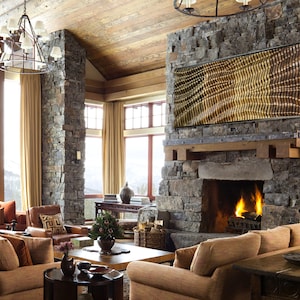 May include: A living room with a stone fireplace and a large window overlooking a snowy mountain view. The room is decorated with brown leather furniture, a wooden coffee table, and a large abstract artwork above the fireplace.