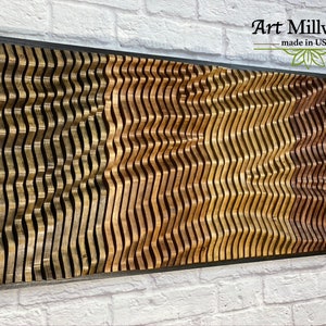 May include: A wooden wall art piece with a wavy pattern in shades of brown, gold, and dark brown. The piece is framed in black and has the text "Art Millwork made in USA" in the top right corner.