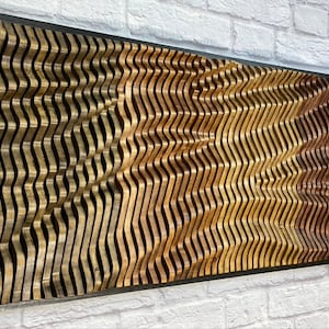 May include: A wall sculpture made of wood with a wavy pattern. The wood is stained in shades of brown, gold, and red. The sculpture is framed in black.