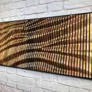 May include: A wall art piece made of wood with a wavy pattern. The wood is a mix of light and dark brown colors. The piece is mounted on a black frame.