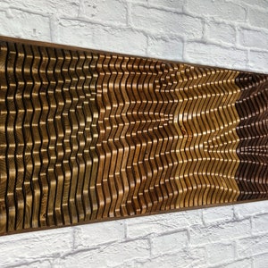 May include: A wall-mounted wooden art piece with a wavy pattern. The piece is made of different shades of brown wood, creating a layered effect.