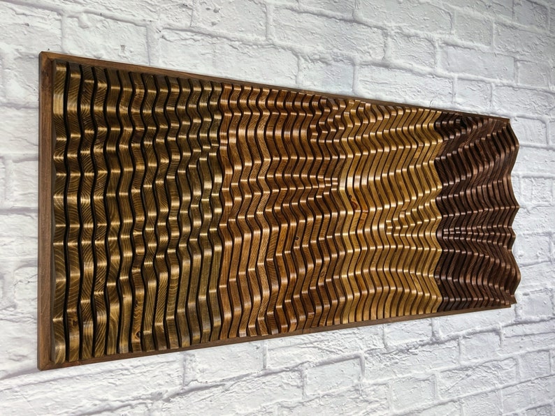 May include: A wall-mounted wooden art piece with a wavy pattern. The piece is made of different shades of brown wood, creating a layered effect.