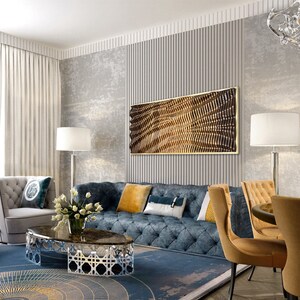May include: A living room interior design with a blue tufted sofa, a coffee table with a marble top and a geometric metal base, two yellow armchairs, and a large abstract wall art piece with a gold frame.