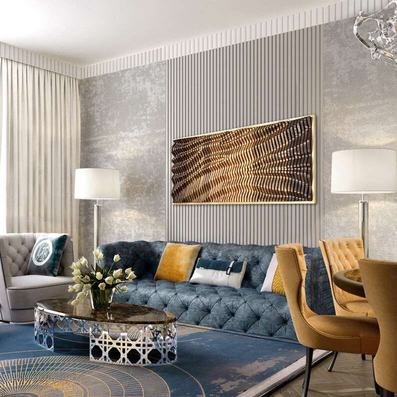 May include: A living room interior design with a blue tufted sofa, a coffee table with a marble top and a geometric metal base, two yellow armchairs, and a large abstract wall art piece with a gold frame.