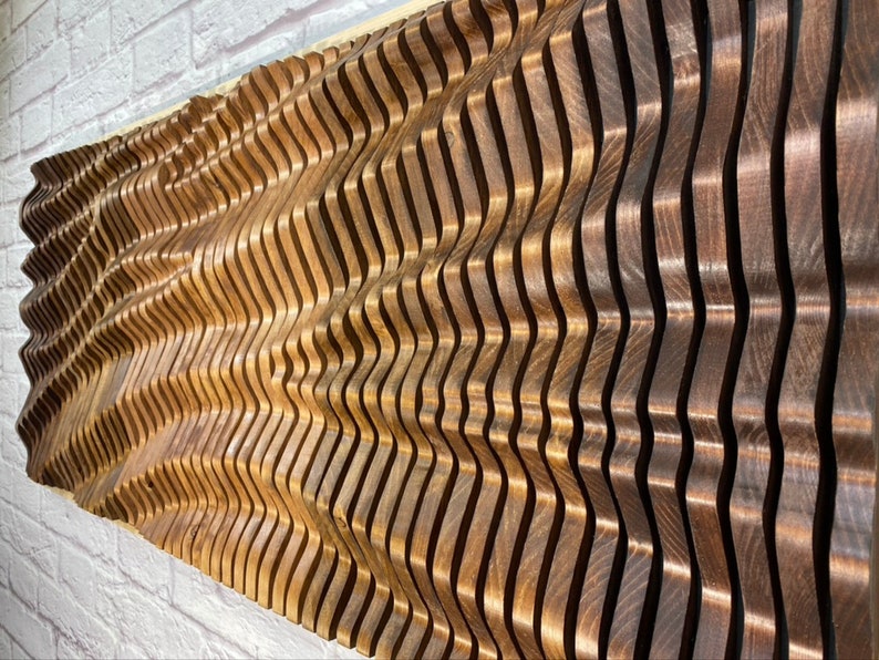 May include: A wall sculpture made of wood with a wavy pattern. The wood is a light brown color and has a natural grain. The sculpture is made up of many individual pieces of wood that are stacked on top of each other.