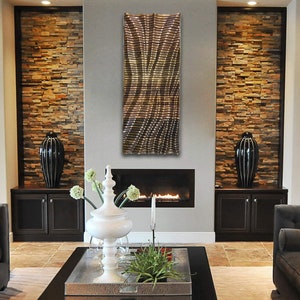 May include: A modern living room with a fireplace and a metal wall sculpture. The fireplace is surrounded by stone and the sculpture is a geometric design in shades of gold and brown.