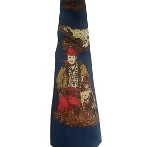May include: A dark blue necktie featuring a repeating pattern of a person wearing a red hat and jacket, sitting in tall grass with a spotted dog. The design includes a second spotted dog running above the person, all set against a subtle geometric background.
