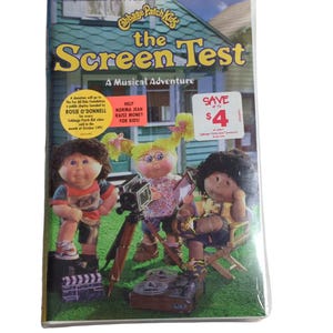 May include: A VHS tape of "Cabbage Patch Kids: The Screen Test - A Musical Adventure." The cover features three Cabbage Patch Kids dolls with a film camera and a clapboard. The tape has a "Save Up To $4" sticker.