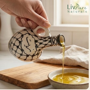 Peut inclure: Un distributeur d'huile d'olive en céramique crème avec un motif de grille noir et une calligraphie arabe, doté d'une anse et d'un bec verseur étroit. Le distributeur verse de l'huile d'olive dorée dans un petit bol, avec le texte LivPure Naturals.
