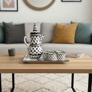 May include: A ceramic coffee set featuring a tall, lidded pot and five small cups, all decorated with a black and white lattice pattern. The set is arranged on a rectangular tray, showcasing a consistent geometric design across all pieces.