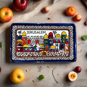 May include: A rectangular ceramic tray with a deep blue border and a central illustration of the city of Jerusalem. The design features colourful buildings with domes, arches, and palm trees, with the word JERUSALEM printed in black capital letters.