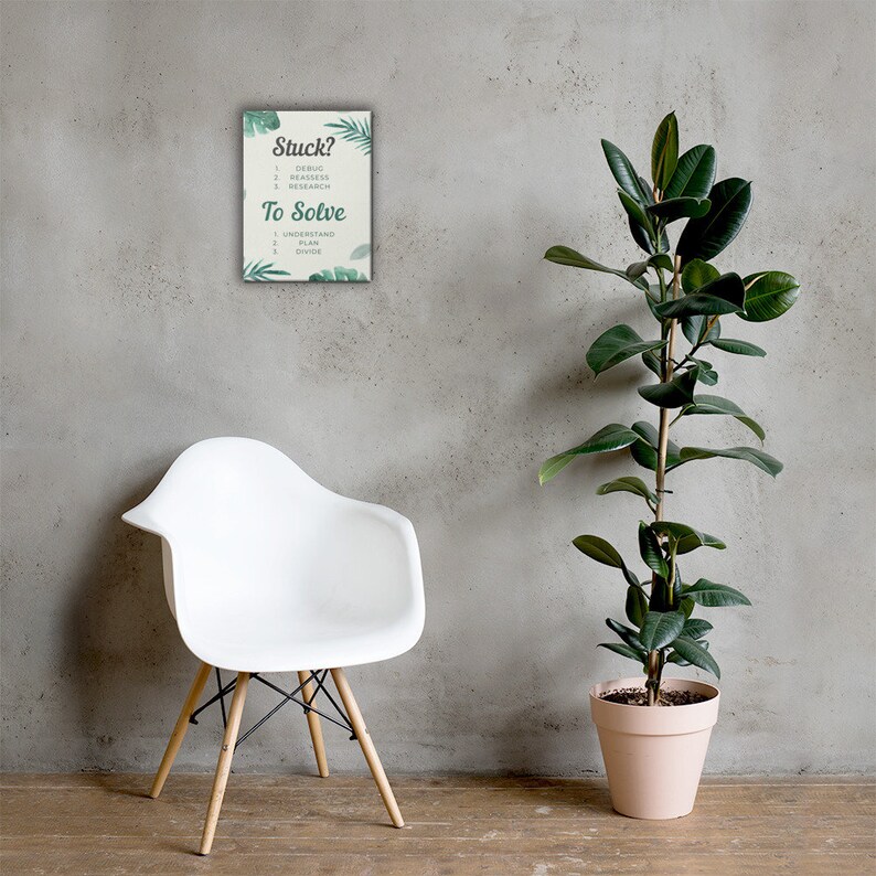 May include: A framed print with the text "Stuck?" and "To Solve" with a list of steps. The print is decorated with green leaf illustrations. A white chair with wooden legs is in front of a gray wall. A tall potted plant is to the right.