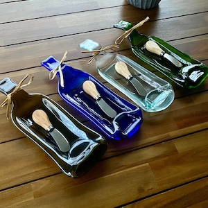 Puede incluir: Cuatro platos de servir de botella de vidrio de diferentes colores con espátulas de madera. Los platos están hechos de botellas de vino recicladas y son perfectos para servir queso, galletas o otros aperitivos.