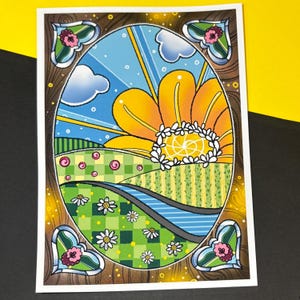 May include: A vibrant art print depicting a large yellow flower against a blue sky with clouds and sun rays. The landscape includes green fields, a winding road, and daisies. The print is framed with a brown border and heart-shaped floral accents, evoking a cheerful, summery scene.