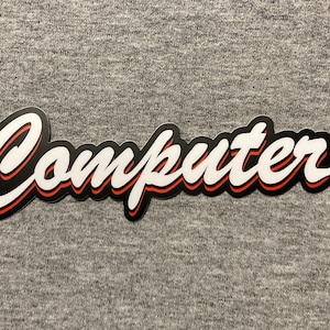 May include: A sticker with the word "Computer" in a stylized script font. The text is white with a black outline and a red shadow, set against a gray background.