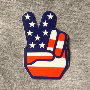 May include: A peace sign sticker with the American flag design. The sticker is blue, red, and white with white stars on the blue background.
