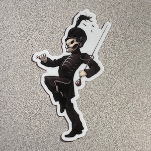 May include: A sticker featuring a cartoon illustration of a marching band member with a skull face. The character is dressed in a black uniform with white accents, holding a baton and a decorative item. The sticker has a white border and is set against a gray background.