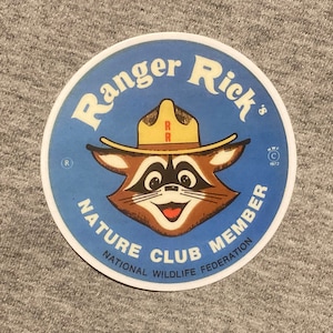 May include: A blue and white round sticker with the text "Ranger Rick's Nature Club Member National Wildlife Federation" and a cartoon raccoon wearing a ranger hat.