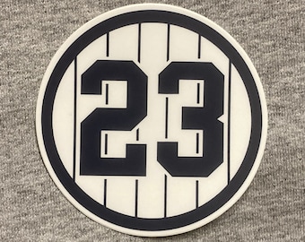 May include: A white circle with a black outline and black stripes. The number 23 is printed in black inside the circle.