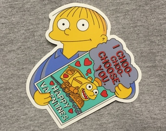 May include: A yellow cartoon character holding a Valentine's Day card with a train and the text "I Choo-Choo Choose You."
