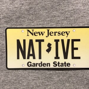 Pu&ograve; includere: Targa gialla con testo nero. In alto si legge "New Jersey", al centro "NATIVE" con la sagoma del New Jersey e in basso "Garden State".