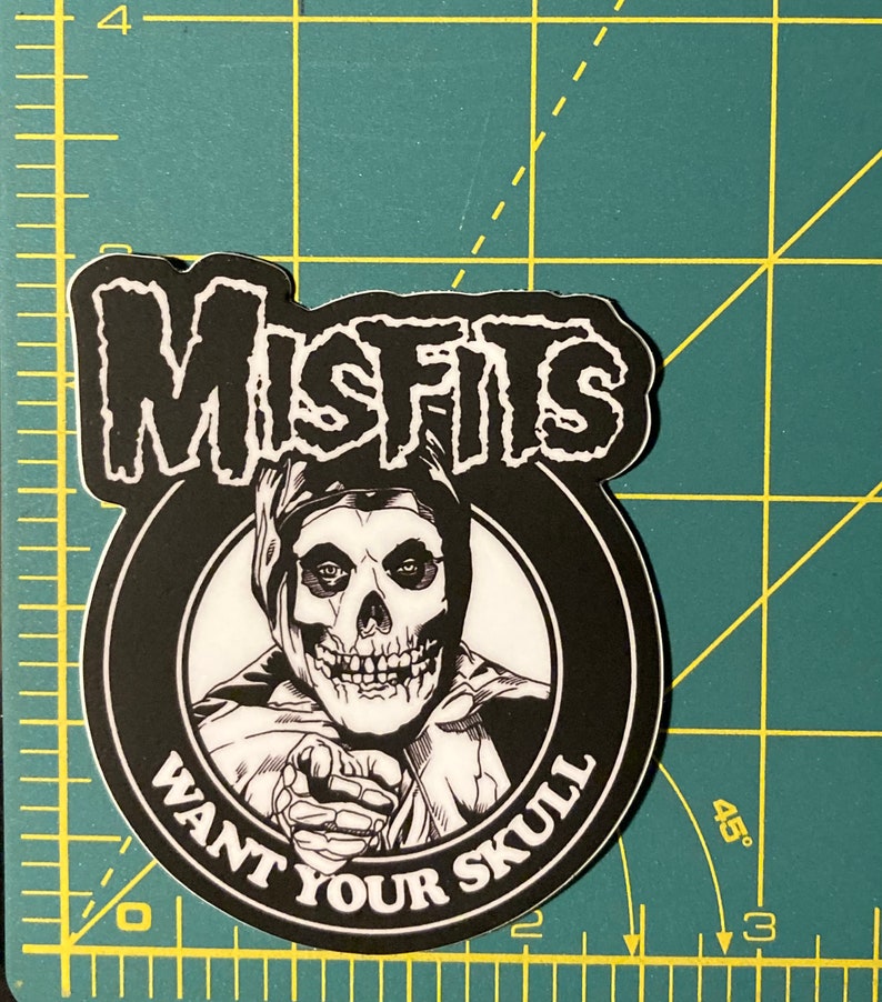 May include: Black and white sticker featuring the Misfits band logo with a skull wearing a hooded robe and the text "Want Your Skull".