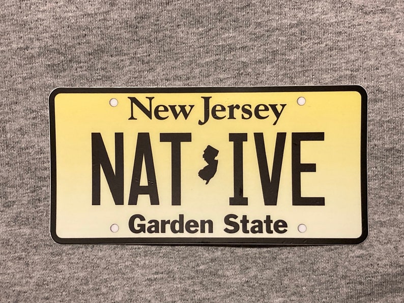 Pu&ograve; includere: Targa rettangolare con sfondo sfumato giallo. Le parole "New Jersey" e "Garden State" sono stampate in nero. La parola "NATIVE" &egrave; anch'essa stampata in nero, con un contorno nero dello stato del New Jersey al centro.