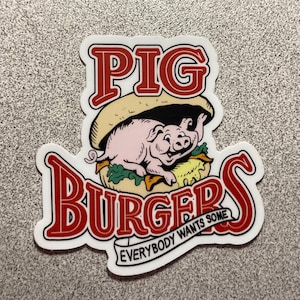 May include: A sticker featuring a cartoon pig in a burger. The text "PIG BURGERS" is in red letters with a white outline. Below, a banner reads "EVERYBODY WANTS SOME". The pig is pink and smiling.