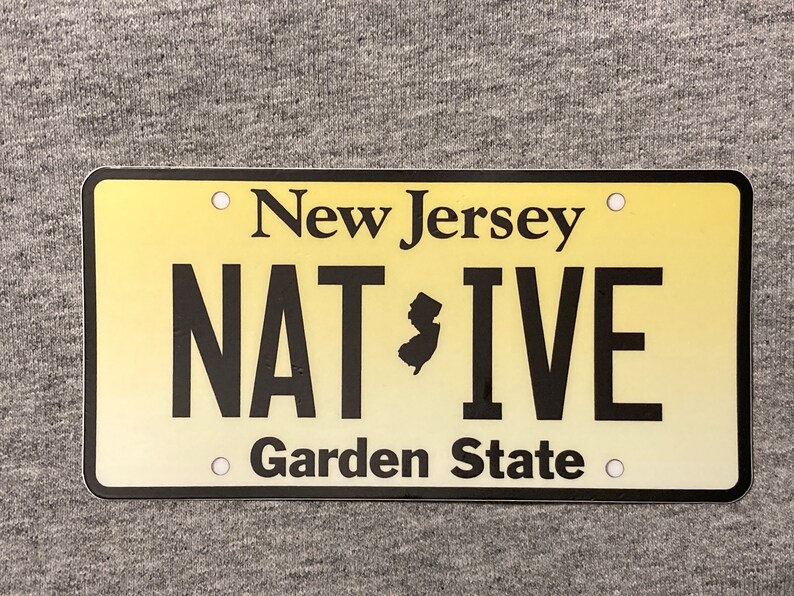 Pu&ograve; includere: Targa rettangolare con sfondo sfumato giallo. Le parole "New Jersey" sono in alto, con "NATIVE" e "Garden State" in basso. Una silhouette nera dello stato &egrave; tra "NAT" e "IVE".