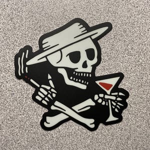 May include: Black and white sticker featuring a skeleton wearing a fedora and holding a martini glass with a red liquid. The skeleton is smoking a cigarette and has crossed bones below.