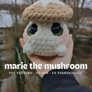 May include: A crocheted mushroom plush toy with a brown cap and white body. The toy has large green eyes and a pink blush on its cheeks. The toy is being held by a hand wearing a black sweatshirt. The text "marie the mushroom" and "PDF PATTERN. NO SEW. US TERMINOLOGY" is below the toy.