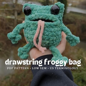 Könnte beinhalten: Eine grüne, gehäkelte Frosch-förmige Kordeltasche mit schwarzen Augen und einer rosa Zunge. Die Tasche wird von einer Hand gehalten. Der Text "drawstring froggy bag" steht unter der Tasche. Der Text "PDF PATTERN - LOW SEW - US TERMINOLOGY" steht unter der ersten Textzeile.